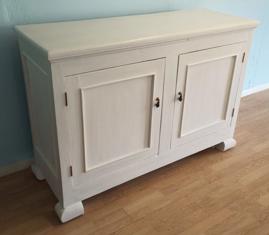 Aparador-despensa de estilo provenzal shabby chic en madera de color blanco marfil con dos puertas y molduras decorativas.