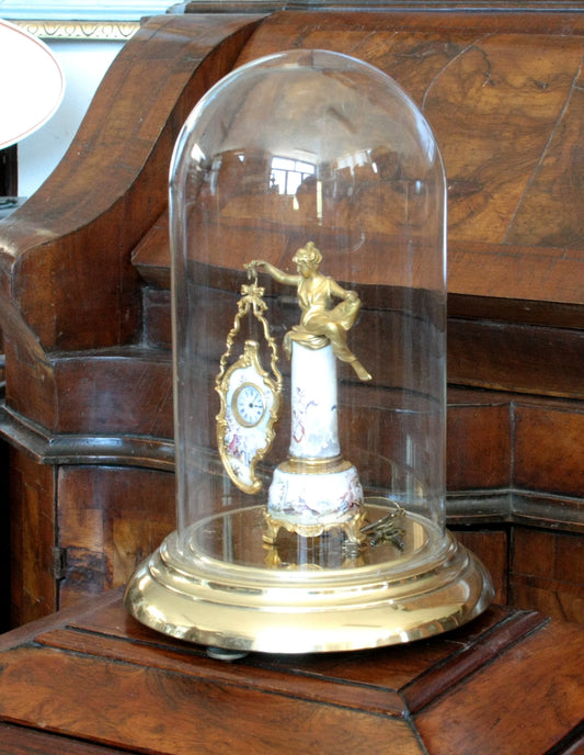 Reloj de mesa de bronce con esmaltes bajo una cúpula de cristal del siglo XIX, base con una escena galante y una figura femenina.