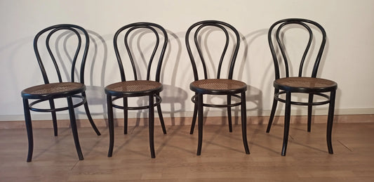 Cuatro sillas de comedor negras de madera de haya curvada, del estilo Thonet Italia, dispuestas en fila.